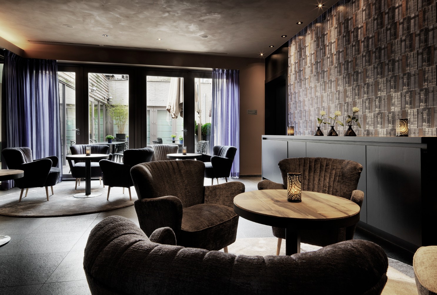 Chique hotel lobby lounge met moderne zitplaatsen, decoratieve bakstenen accentmuur en sfeervolle verlichting.